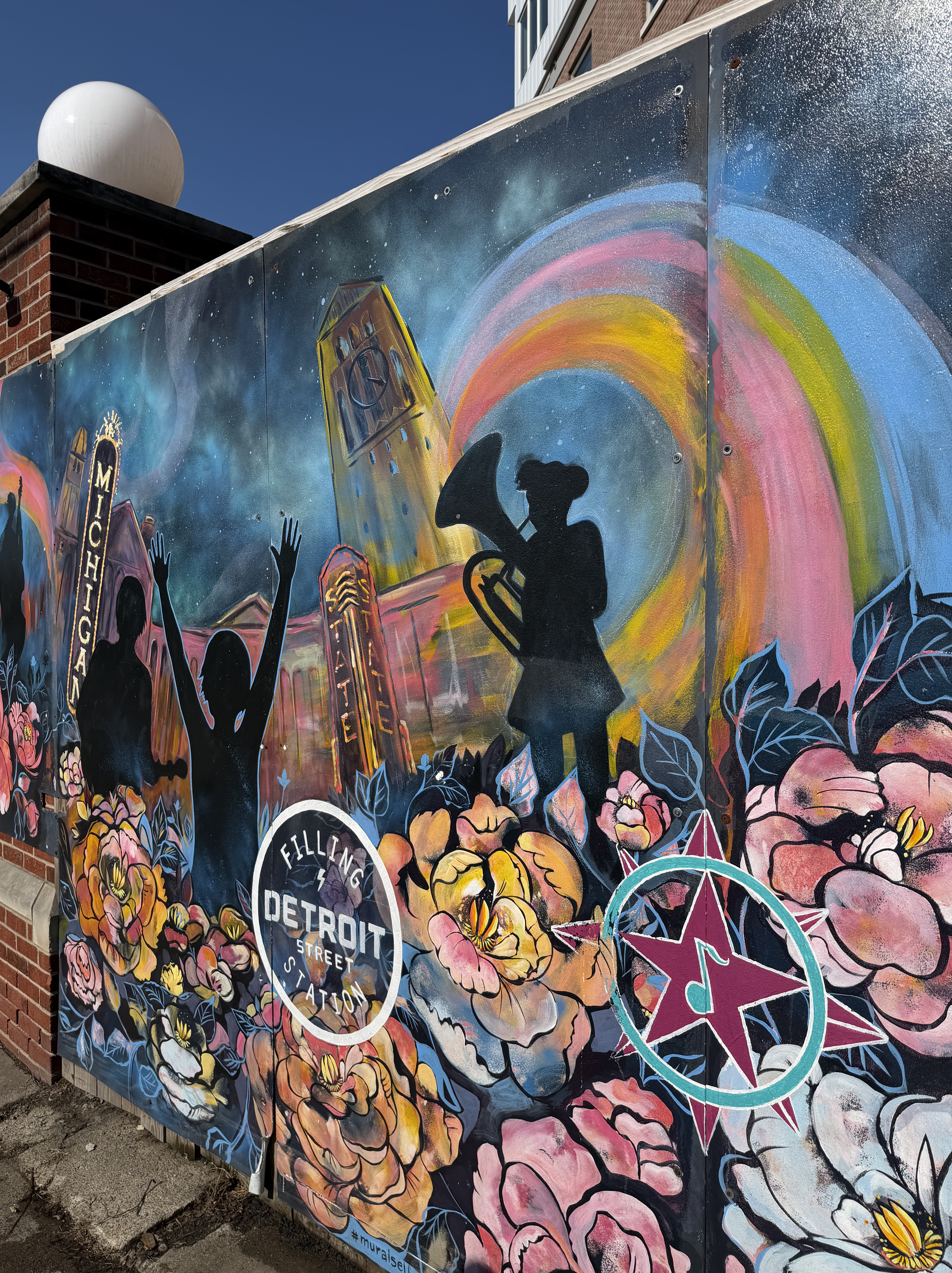 An outside mural of Burton Memorial Clocktower, a rainbow, the infamous Michigan theater sign on E. Liberty, and shadowed figures playing instruments. The DSFS logo is pictured at the bottom.